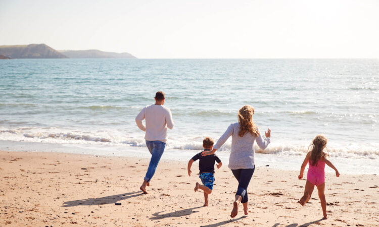Rear View Of Family On Beach Running Across Sand Towards Sea